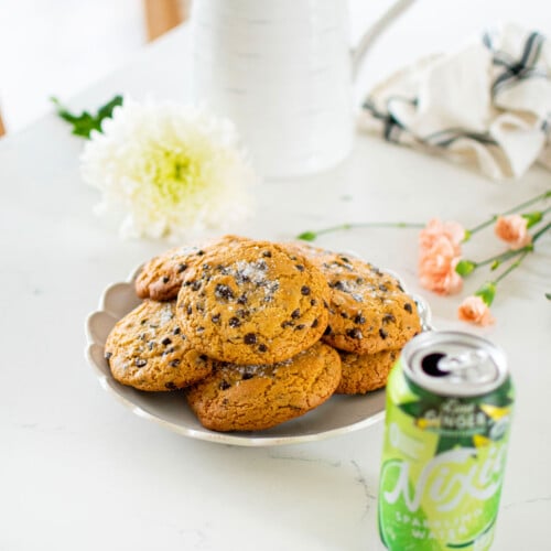plate of olive oil honey chocolate chip cookies on a white marble counter with fresh flowers and a can of sparkling water.