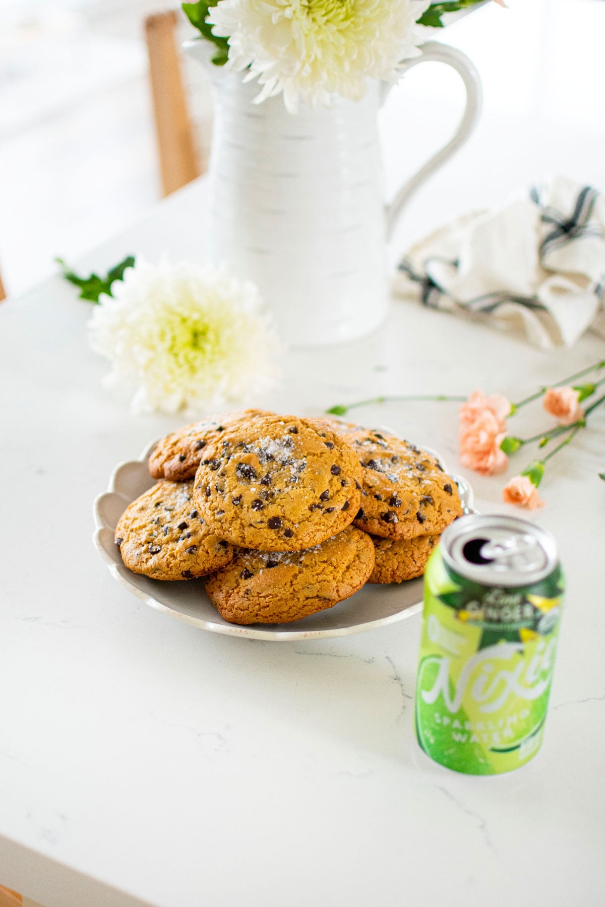 plate of olive oil honey chocolate chip cookies on a white marble counter with fresh flowers and a can of sparkling water.