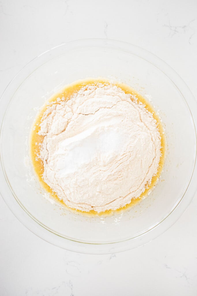 ingredients for olive oil honey chocolate chip cookie dough in a glass mixing bowl on a white marble counter.