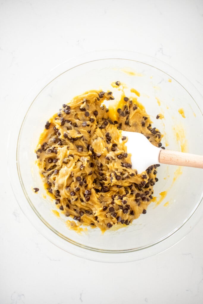 olive oil honey chocolate chip cookie dough in a glass mixing bowl on a white marble counter.