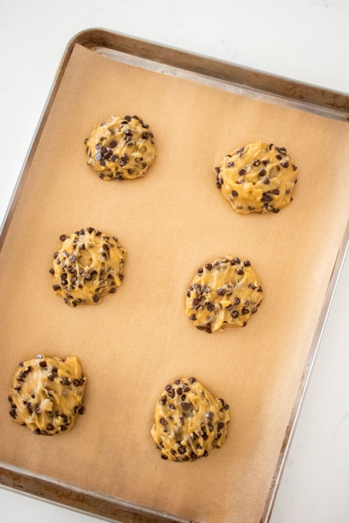 olive oil honey chocolate chip cookie dough balls on a baking sheet on a white marble counter.