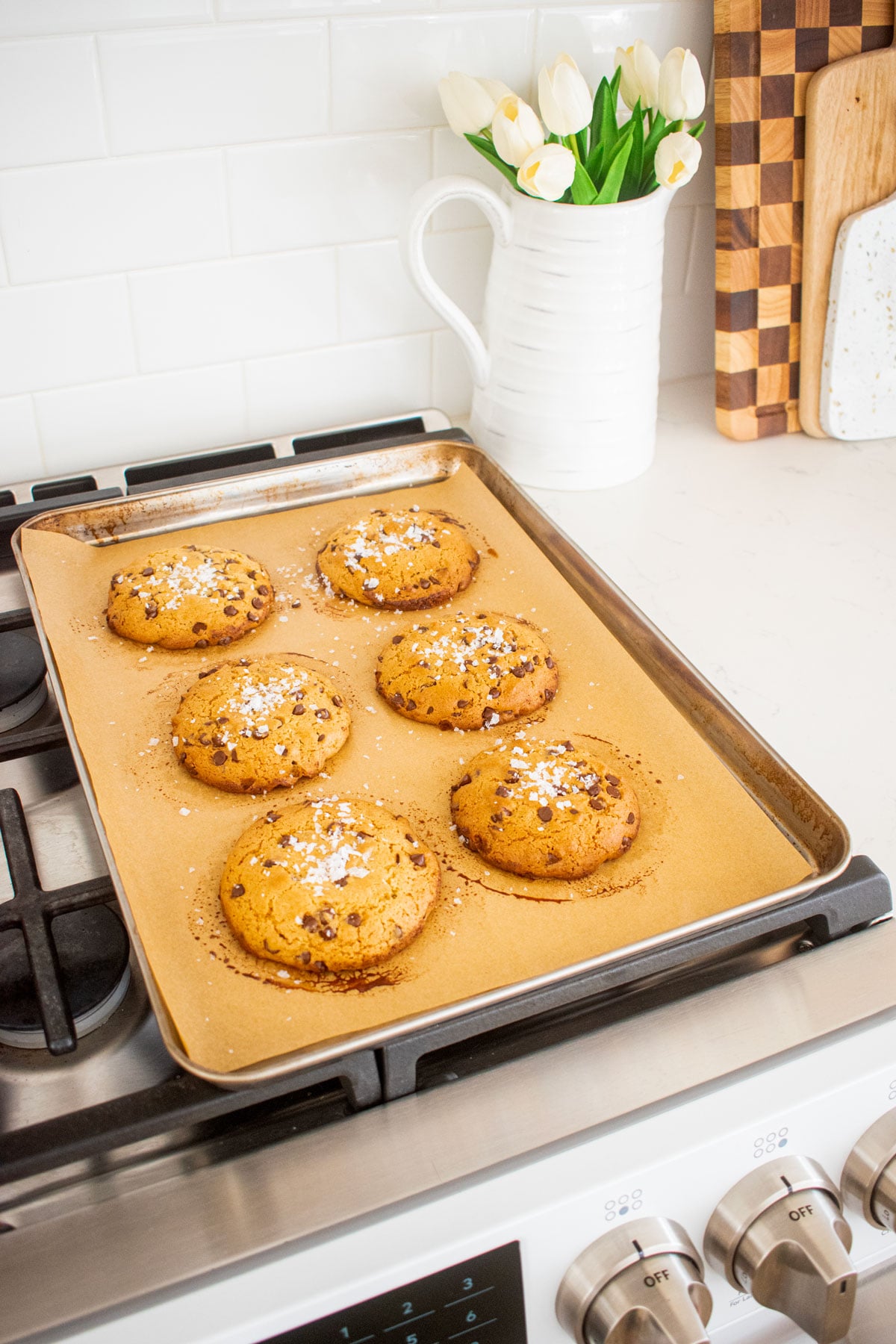 olive oil honey chocolate chip cookies with flaky sea salt on a baking sheet cooling on the oven.