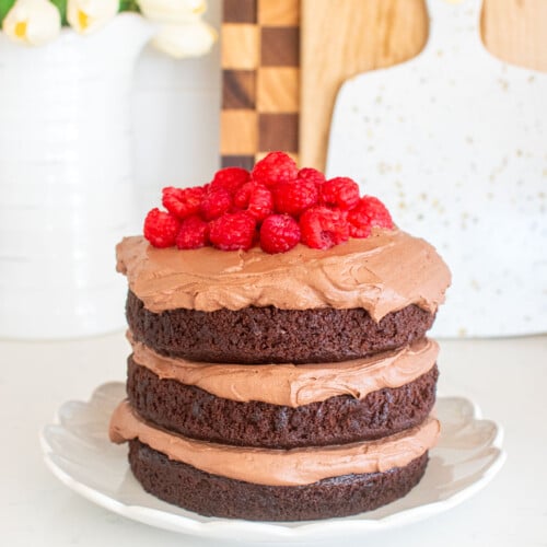 chocolate naked cake with chocolate whipped cream frosting and fresh raspberries on top on a white marble counter.