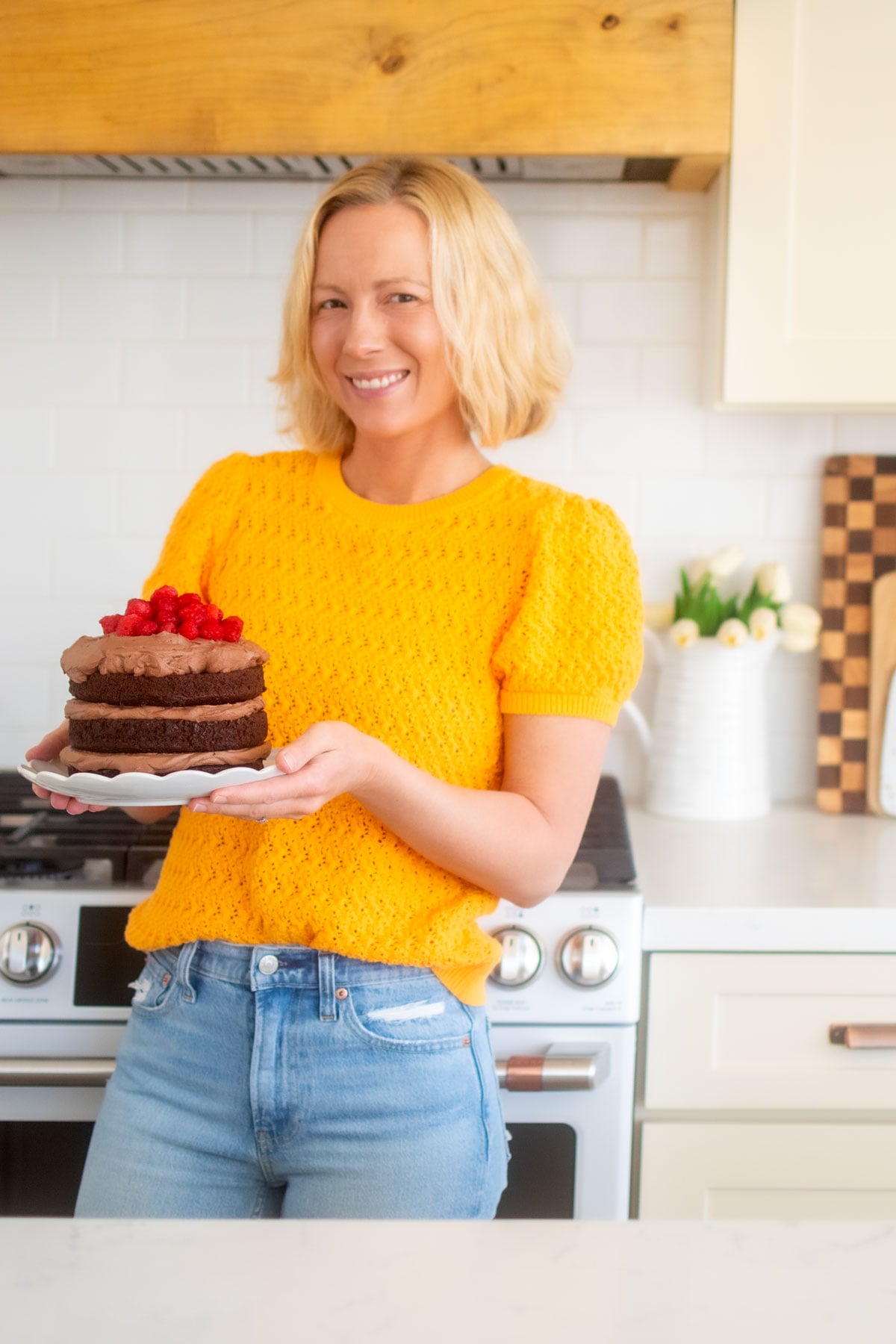 woman holding a chocolate naked cake with fresh raspberries in the kitchen.