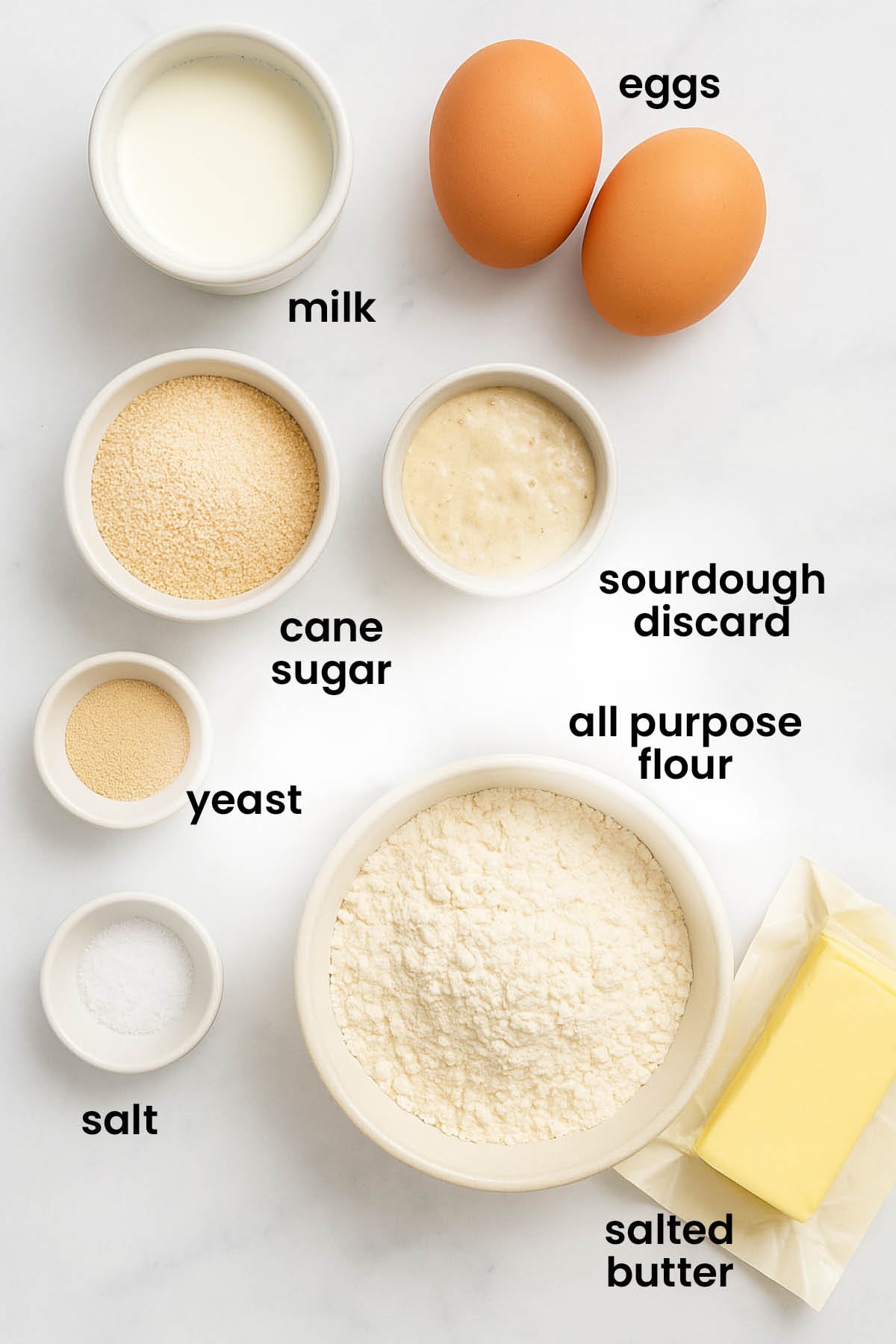 individual ingredients for homemade sourdough hot dog buns laid out against a white background.