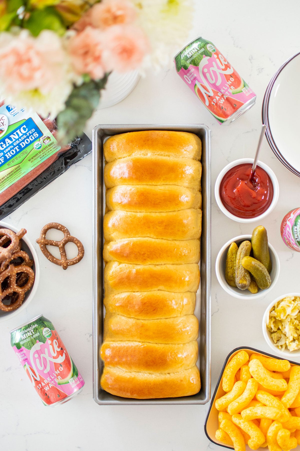 homemade sourdough hot dog buns in a hot dog bun pan on a white marble counter with toppings around.