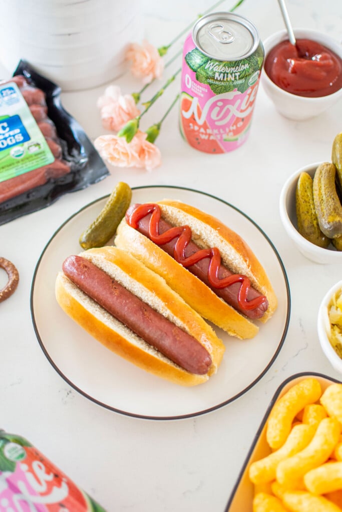 two hot dogs in homemade sourdough hot dog buns on a plate with hot dog toppings around.