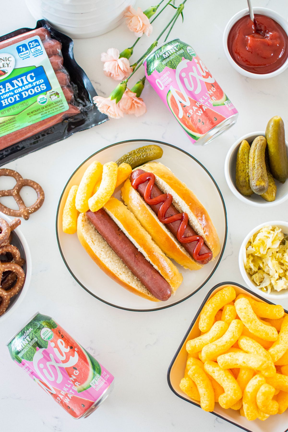 two hot dogs in homemade sourdough hot dog buns on a plate with hot dog toppings around.