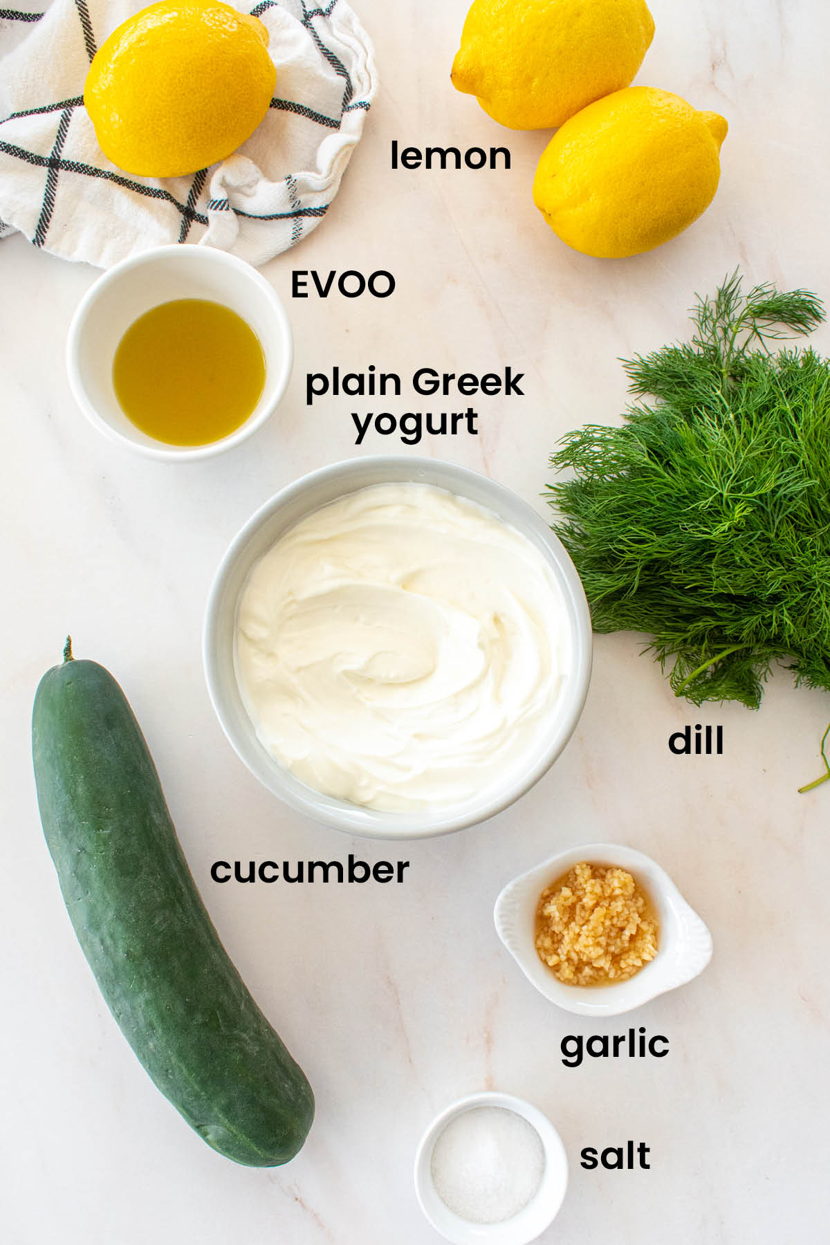 individual ingredients for organic tzatziki sauce with fresh dill laid out against a white background.