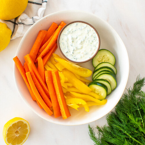 organic tzatziki sauce in a small dish on a platter with veggies on a marble countertop.