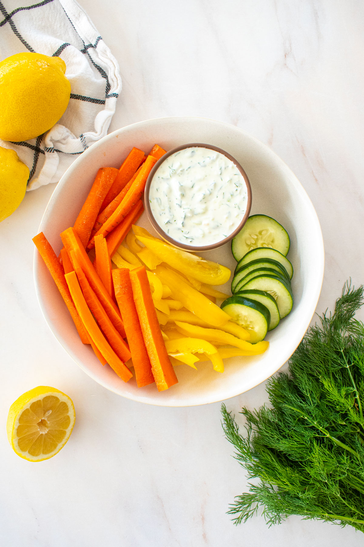 organic tzatziki sauce in a small dish on a platter with veggies on a marble countertop.