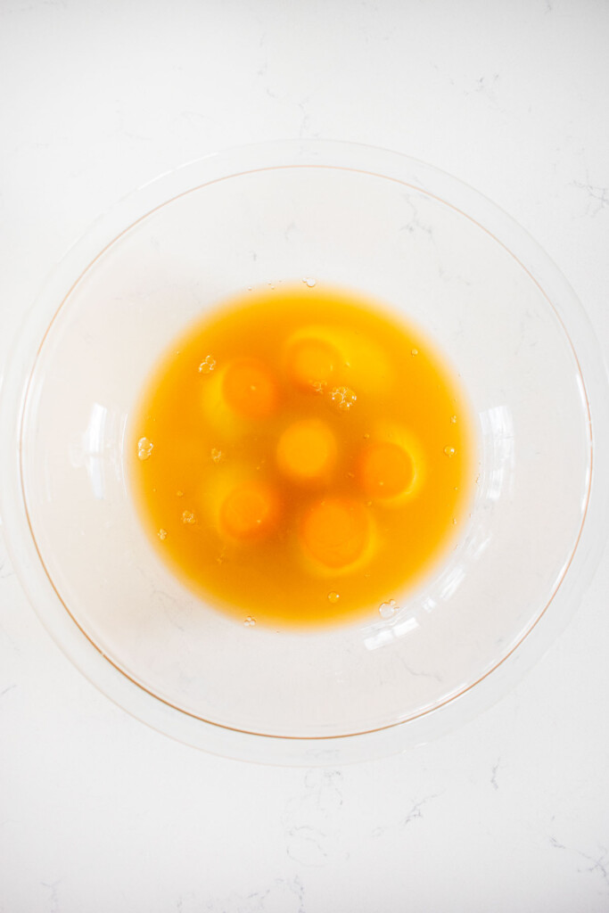 eggs and bone broth in a glass mixing bowl on a marble countertop.
