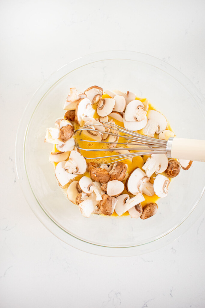 sliced mushrooms, eggs and bone broth in a glass mixing bowl on a marble countertop.