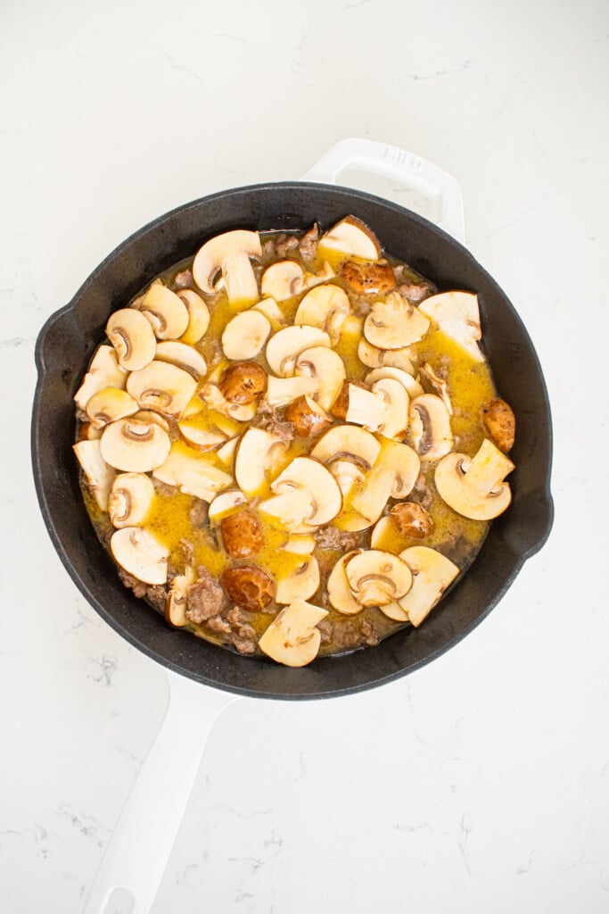 breakfast sausage, eggs, bone broth and mushrooms in a cast iron skillet on a marble countertop.