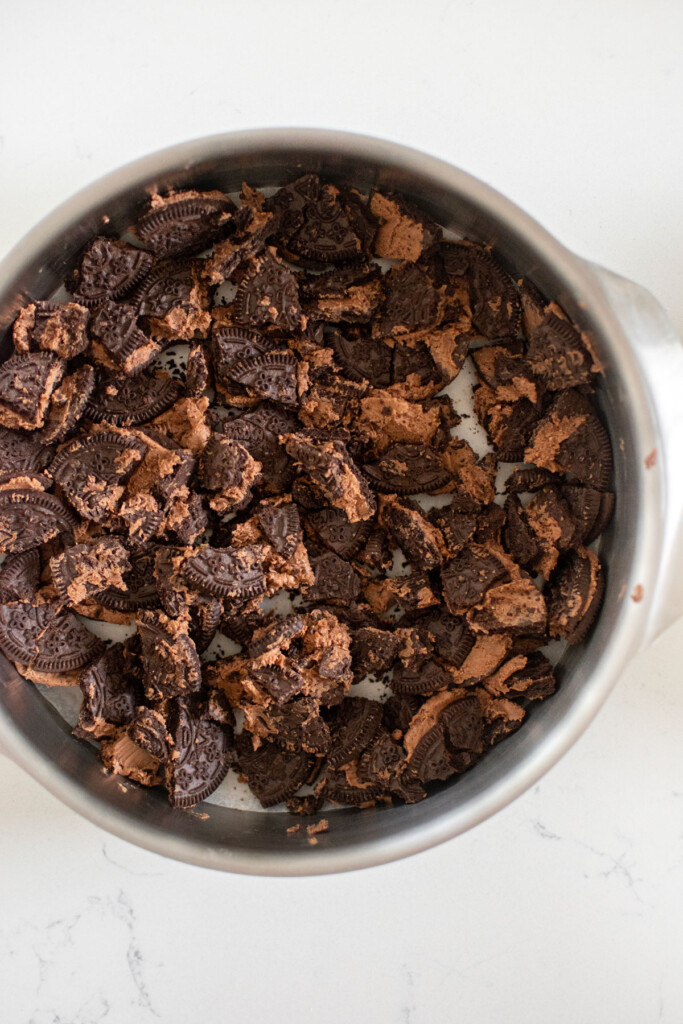 crushed up chocolate oreo cookies in a cake pan on a white marble counter.
