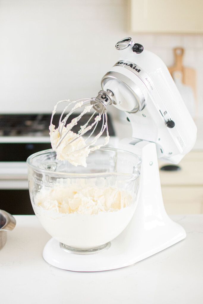 homemade whipped cream in a stand mixer on a white marble counter.