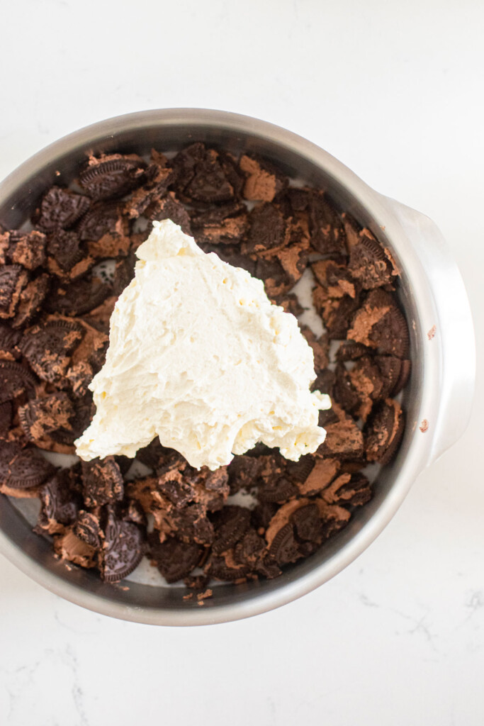 cake pan with crushed up oreos and whipped cream on a white marble counter.