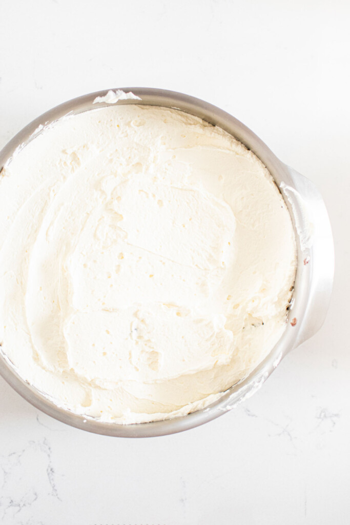 cake pan with whipped cream spread evenly on a white marble counter.