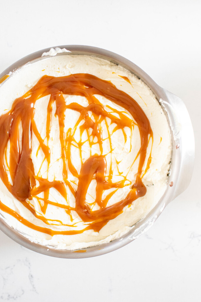 cake pan with whipped cream and swirled caramel sauce on a white marble counter.