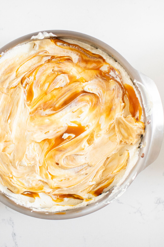 cake pan with whipped cream and swirled caramel sauce on a white marble counter.