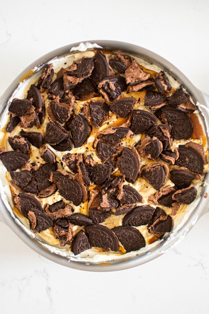 caramel chocolate oreo icebox cake being assembled in a cake pan on a white marble counter.