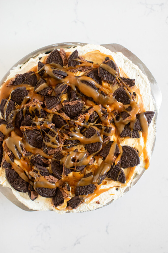 caramel chocolate oreo icebox cake being assembled in a cake pan on a white marble counter.