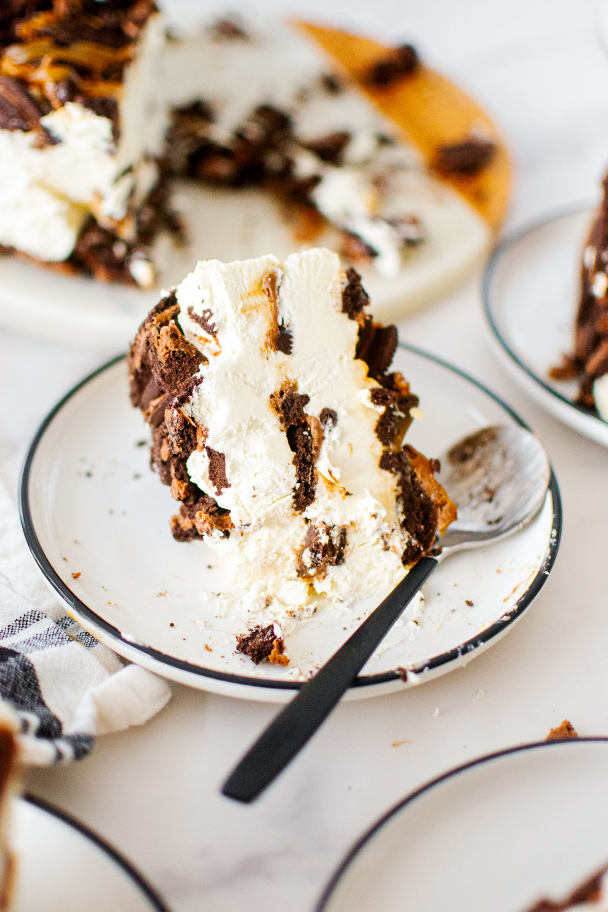 slice of caramel chocolate oreo icebox cake on a plate with a spoon on a white marble table.