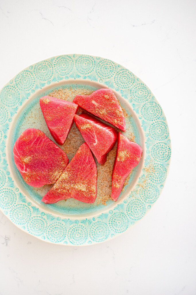 raw ahi tuna with chili lime seasoning on a green plate on a white marble coutnertop.