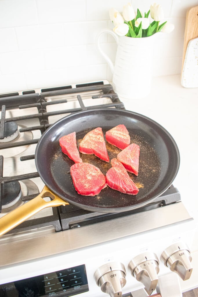 raw ahi tuna with chili lime seasoning in a large skillet on the stovetop.