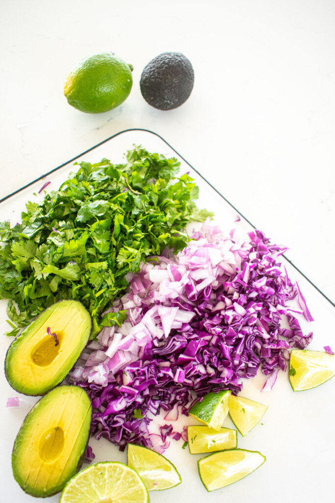 chopped taco toppings on a white cutting board on a white marble countertop.