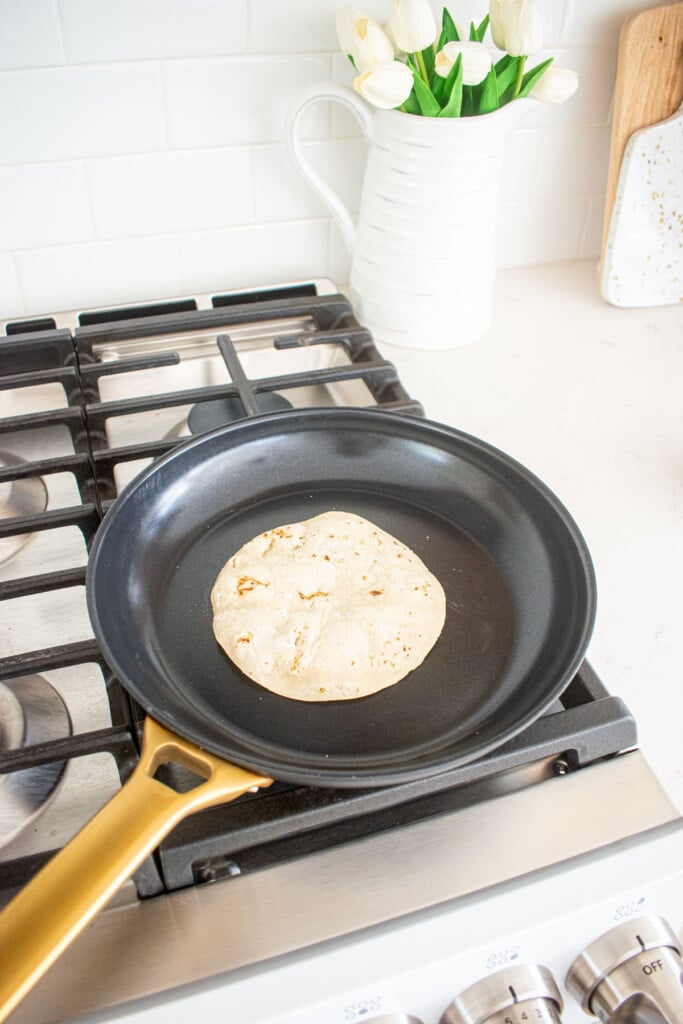 corn tortilla being warmed in a black skillet on the stovetop.