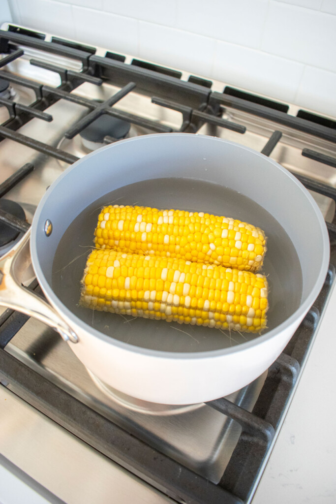 corn on the cob being boiled in a pot on a stovetop.