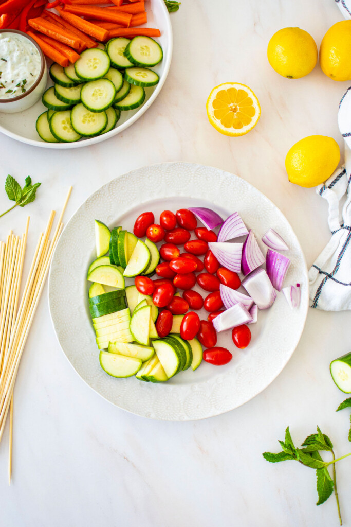 plate with cut zucchini, red onion and grape tomatoes on a white marble countertop.