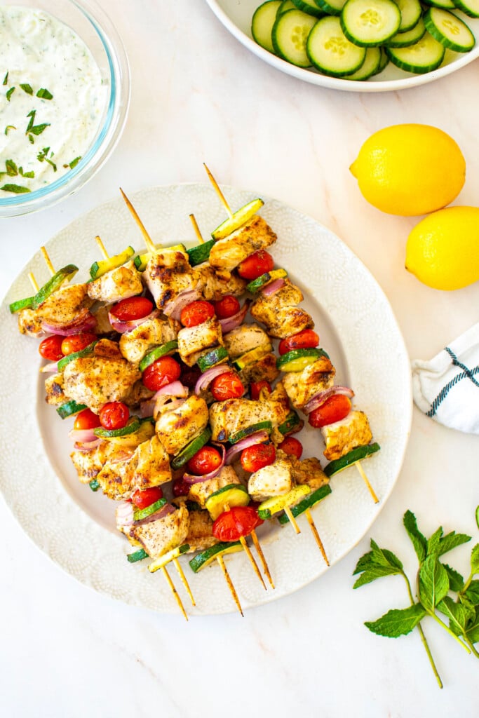 grilled greek chicken shish kabobs on a plate on a white marble countertop.