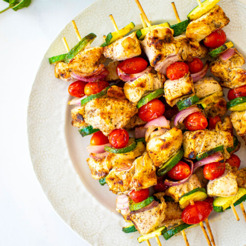 grilled greek chicken shish kabobs on a plate on a white marble countertop.