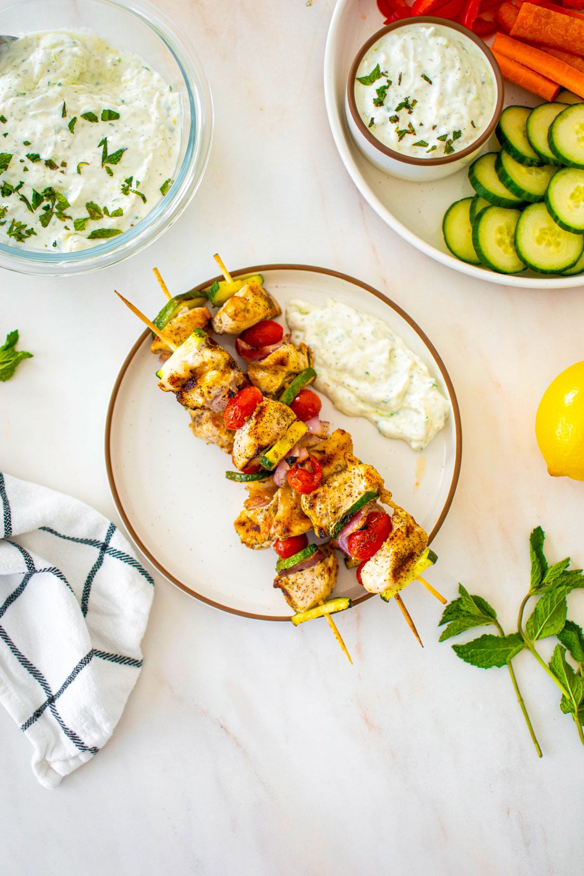 grilled greek chicken shish kabobs on a plate with tzatziki sauce.