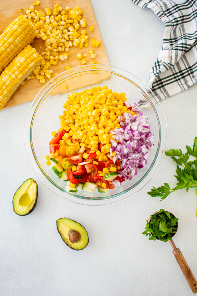 ingredients for real simple corn salad with avocado in a glass mixing bowl on a white countertop.