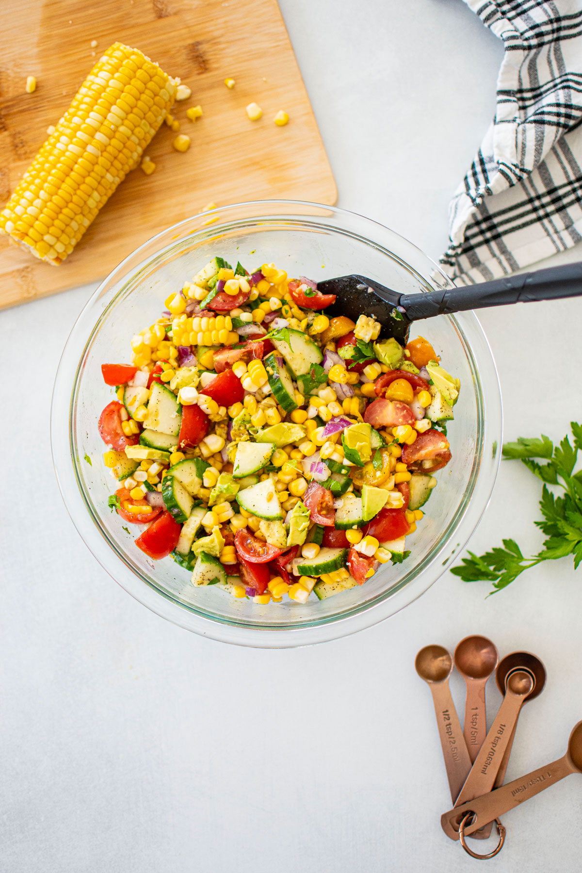 real simple corn salad with avocado being mixed in a glass mixing bowl on a white countertop.