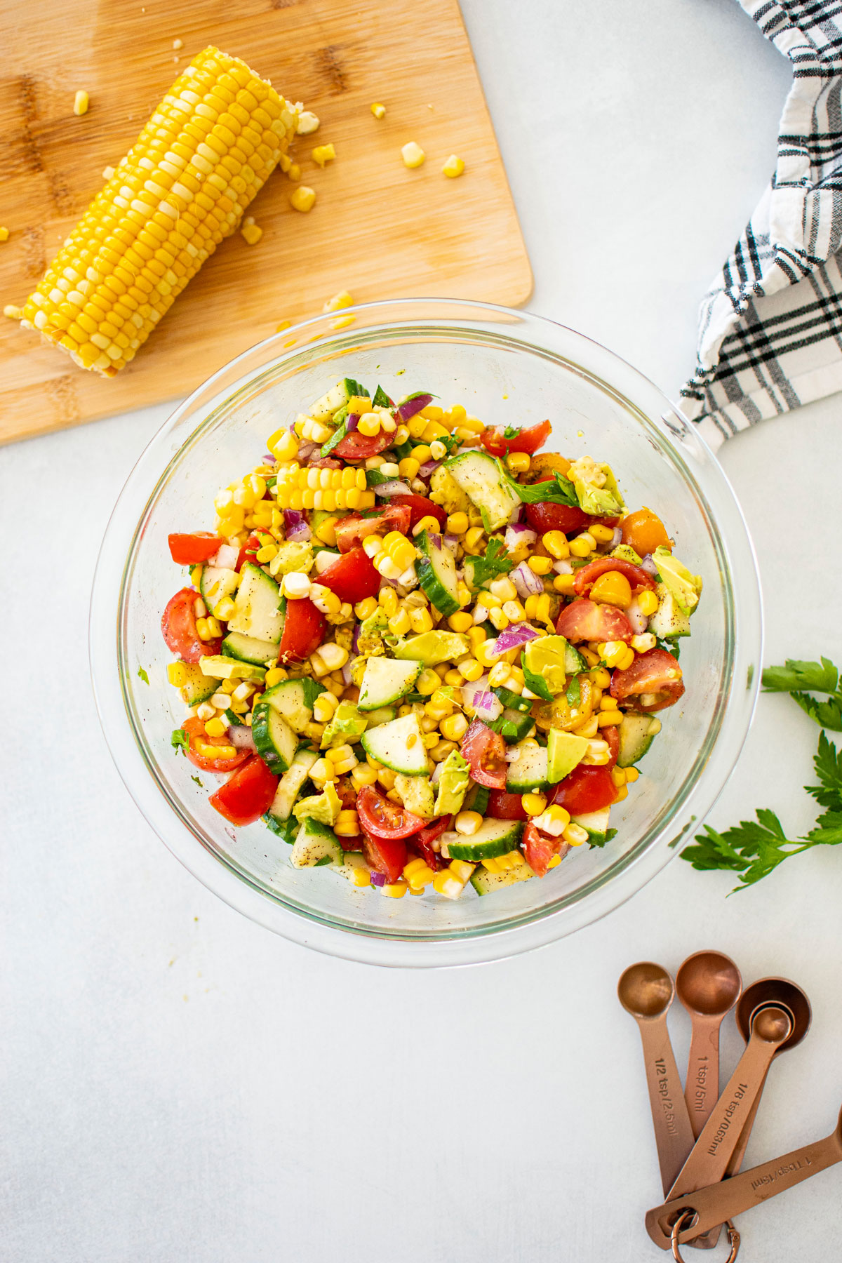 real simple corn salad with avocado in a glass mixing bowl on a white countertop.