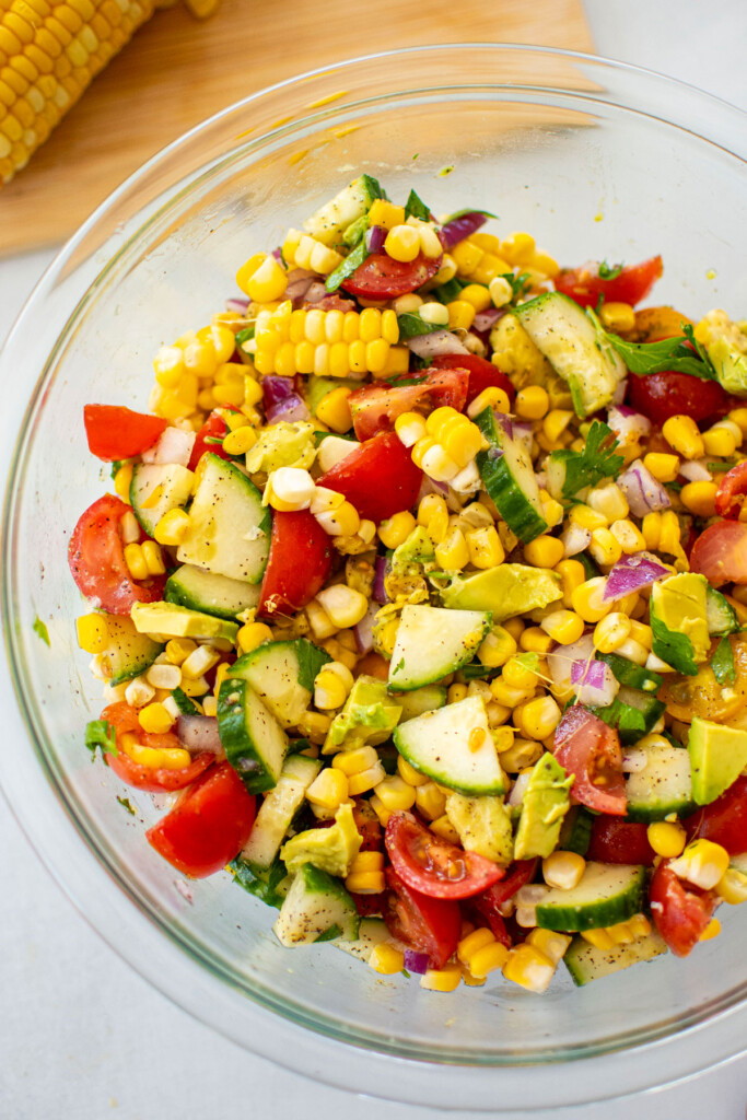 real simple corn salad with avocado in a glass mixing bowl on a white countertop.