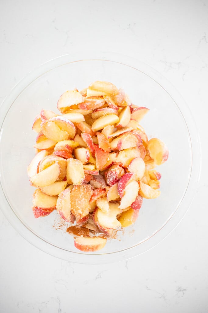 peach pie filling mixed together in a glass mixing bowl on a white marble counter.