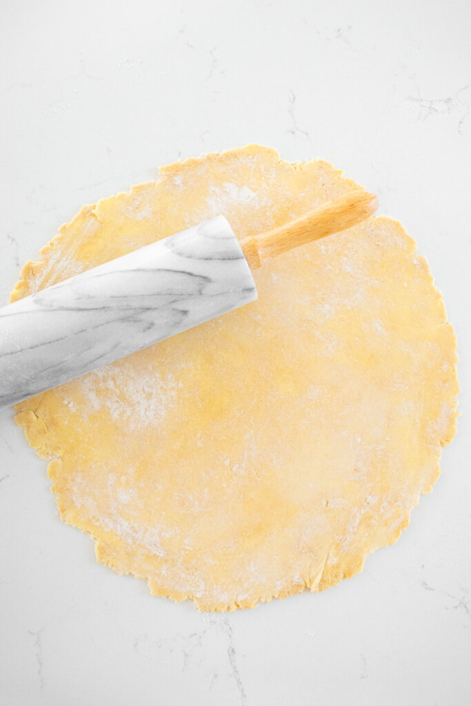 pie crust being rolled out on a white marble counter with a marble rolling pin.
