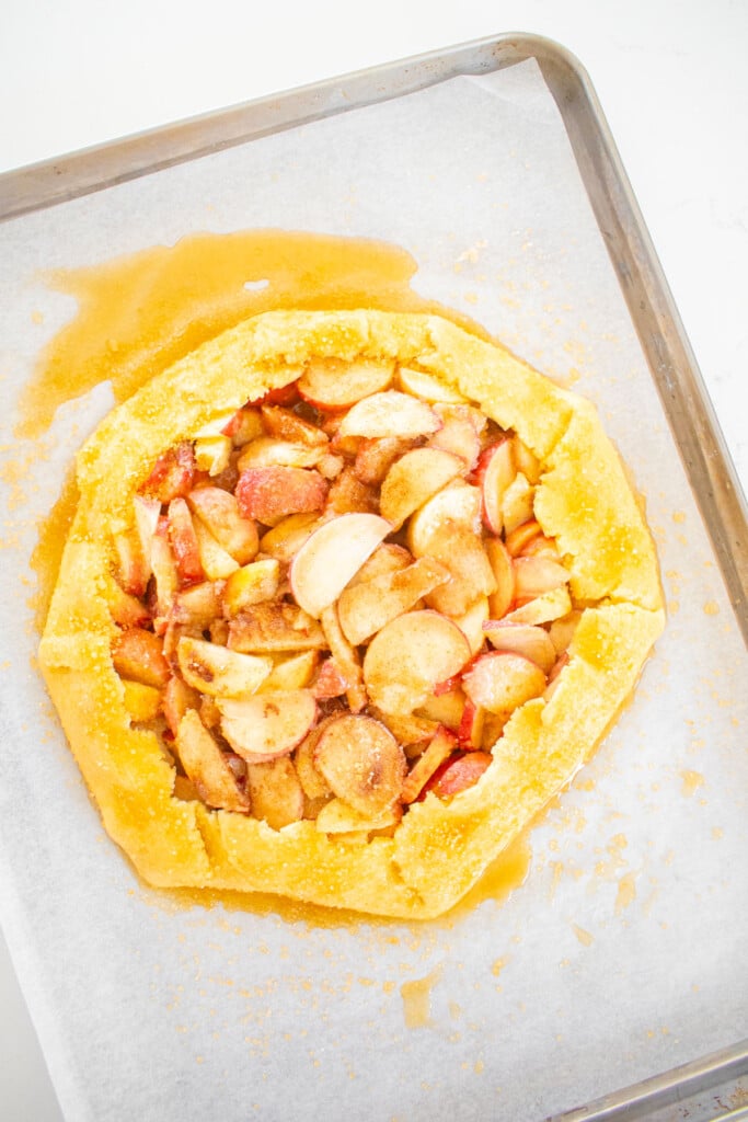 sourdough peach galette on a baking sheet with honey pie wash.