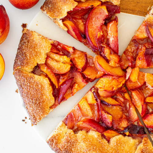 rustic sourdough peach galette cut into slices on a marble serving board.