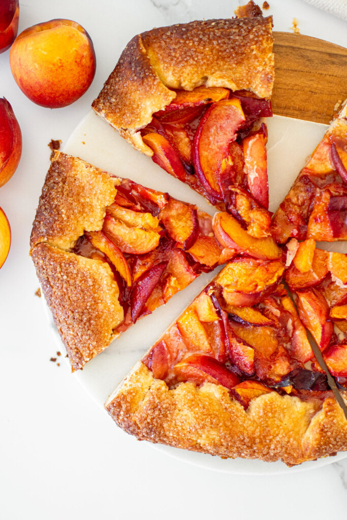 rustic sourdough peach galette cut into slices on a marble serving board.
