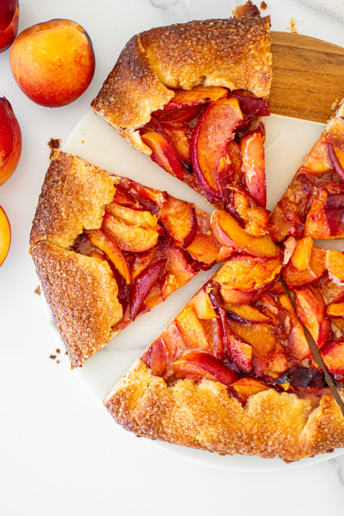 rustic sourdough peach galette cut into slices on a marble serving board.