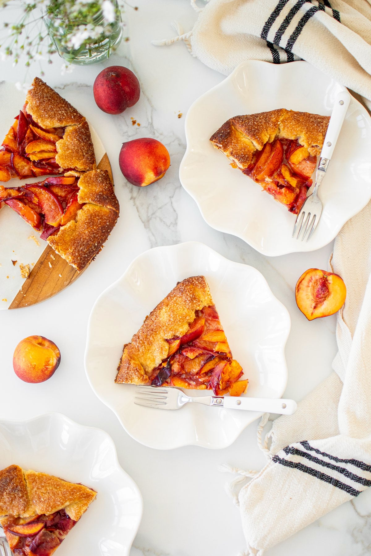 slices of rustic sourdough peach galette on white ruffle plates.