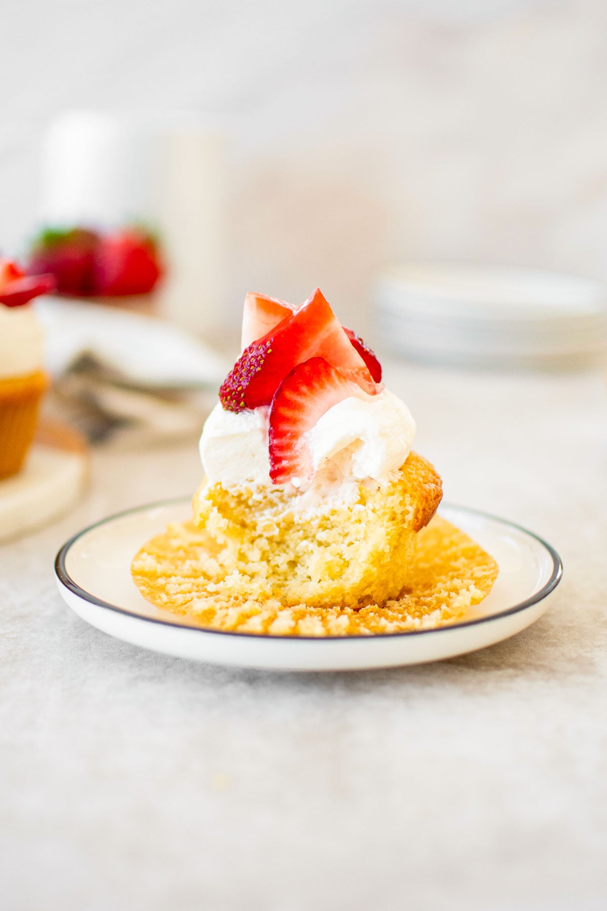 strawberry shortcake cupcake with fresh strawberries with a bite taken out on a plate on a table.