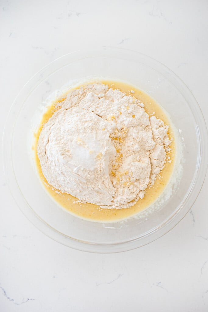 glass mixing bowl with wet ingredients for vanilla cake mixed together and flour on top.