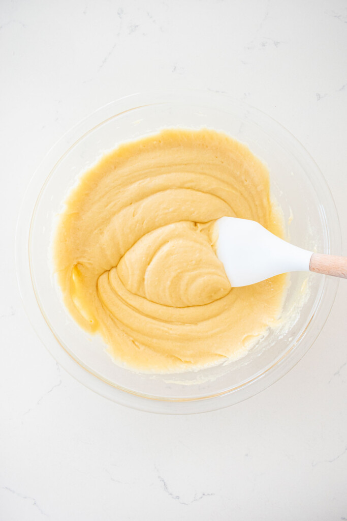vanilla cake batter in a glass mixing bowl on a white marble counter with a spatula.